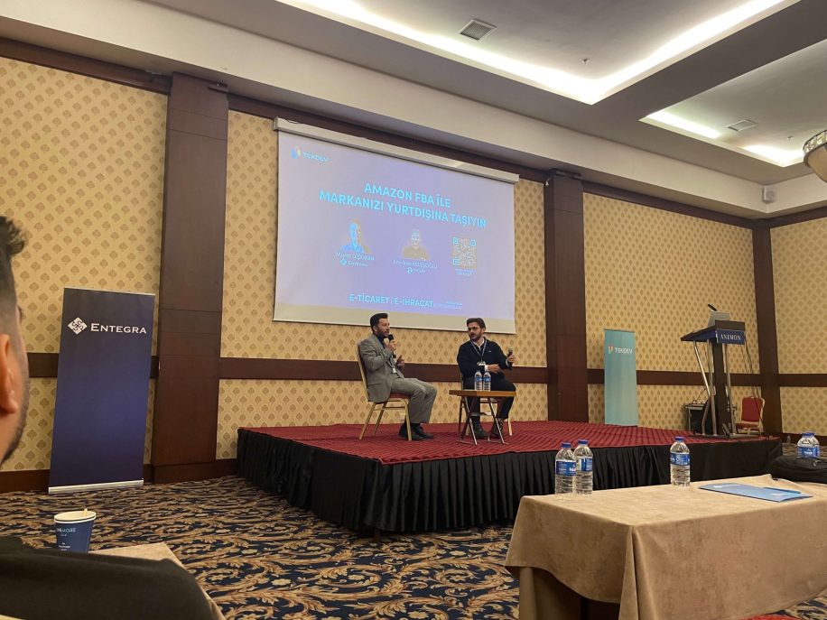 Denizli etkinliğinde sahnede panel oturumu, arkada sunum ekranı